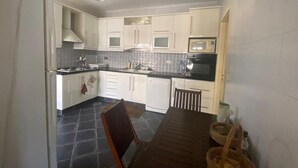 Une cuisine compacte avec des meubles blancs, un four à micro-ondes, un four traditionnel et une table à manger avec des chaises.