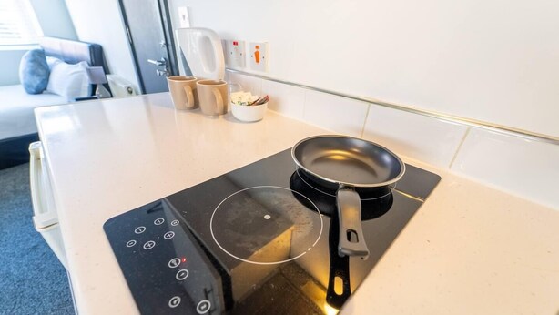 Una cocina con placa de inducción, sartén y cafetera.