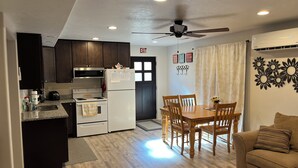 A compact kitchen with dark cabinets, a white refrigerator, a stove, and a ceiling fan.