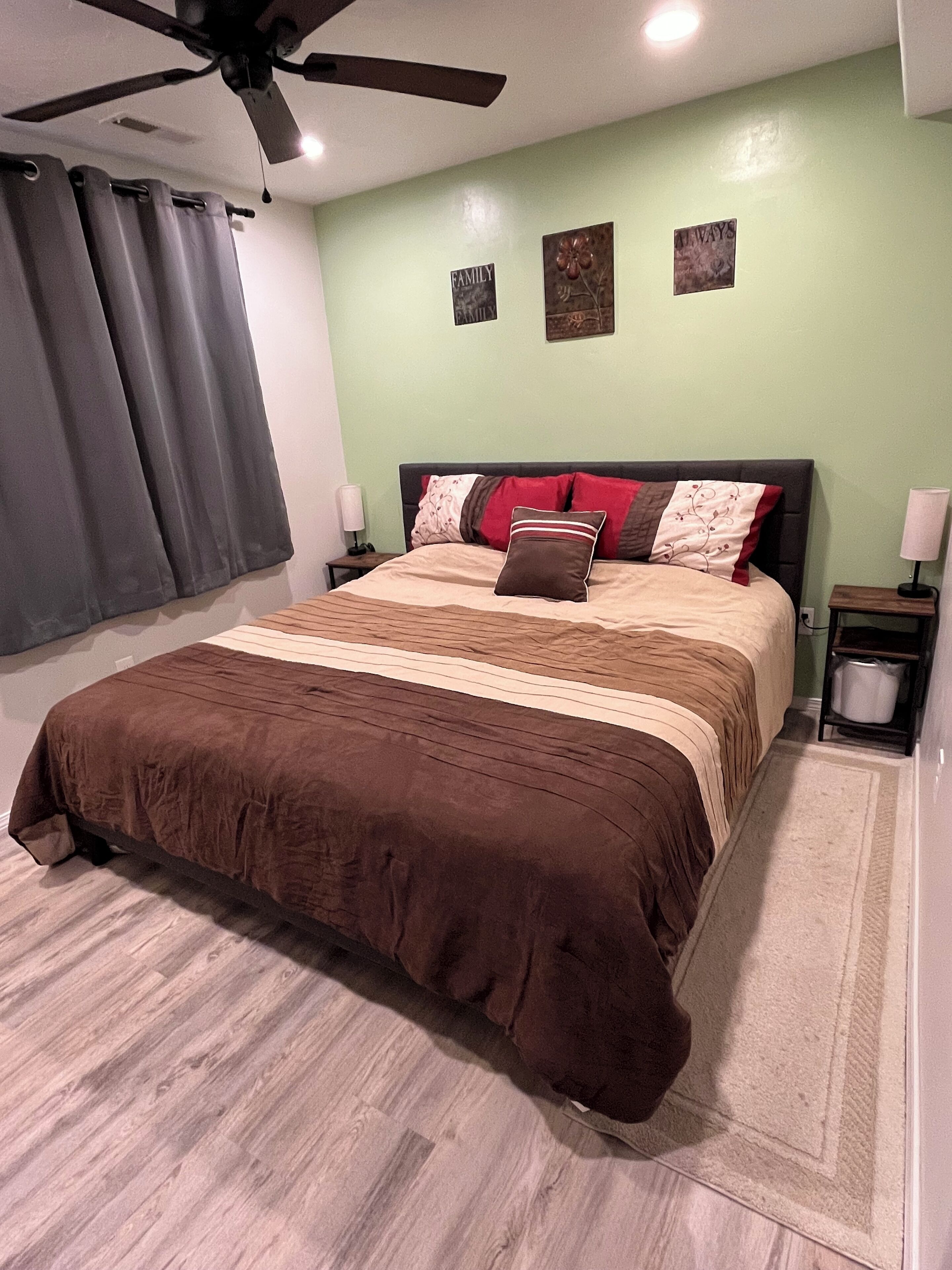 Une chambre à coucher avec un lit, un ventilateur de plafond, une table de chevet avec une lampe et un mur orné de deux tableaux encadrés.