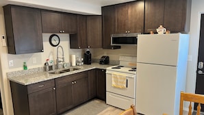 A modern kitchen with dark wood cabinets, a granite countertop, a stainless steel sink, a stove, and a refrigerator.