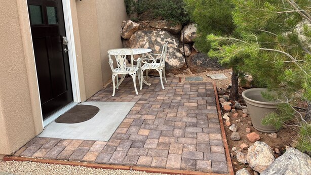 A patio with a brick floor, white metal chairs, and a door.