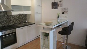 A modern kitchen with white cabinets, a black stove, and a glass island with bar stools. - Apartment at Sulzbach (Sulzburg)
