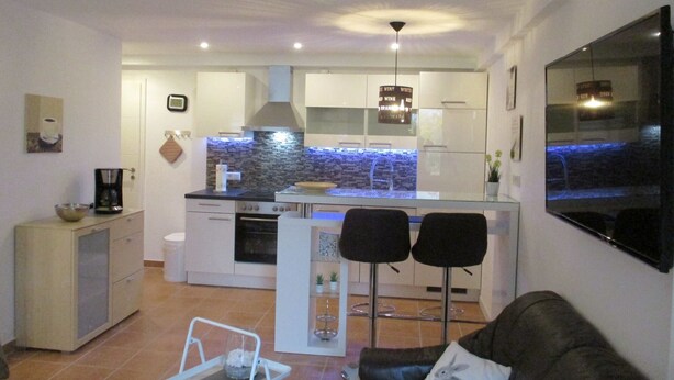 A modern kitchen with a central island, a dining area with two chairs, a sofa with a cushion, and a TV mounted on the wall. - Apartment at Sulzbach (Sulzburg)