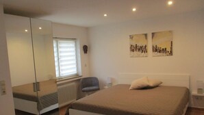 A bedroom with a bed, a chair, a radiator, a window with blinds, and two wall-mounted paintings. - Apartment at Sulzbach (Sulzburg)