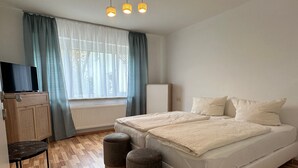 A bedroom with a bed, two ottomans, a TV on a cabinet, and a window with curtains. - Apartment "Dreams im Obergeschoss" with Private Terrace & Wi-Fi (Kötz)