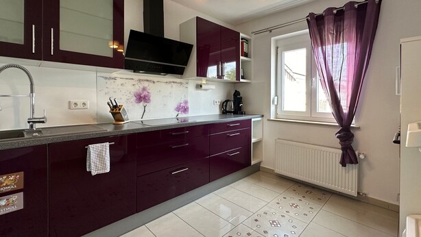 A modern kitchen with dark cabinets, a stainless steel sink, and a window with purple curtains. - Apartment "Dreams im Obergeschoss" with Private Terrace & Wi-Fi (Kötz)