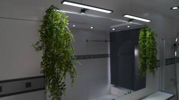 A modern bathroom with a large mirror, hanging plants, and recessed lighting.