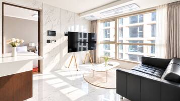 A modern hotel room with a large window, a flat-screen TV, a black leather sofa, and a marble floor.