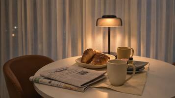 A round table with a newspaper, a plate of croissants, a mug, and a lamp.