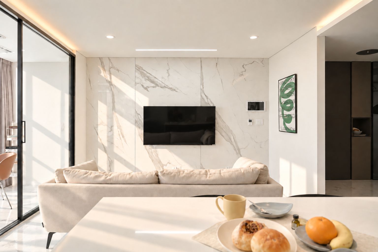Una sala de estar moderna con una pared de mármol, un televisor montado, un sofá, una mesa de comedor con una taza de café y un frutero.