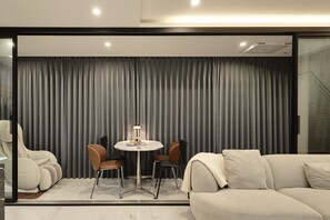 A modern living room with a sofa, chairs, a table, and a large grey curtain.