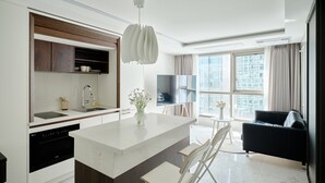 A modern kitchen with a central island, built-in appliances, and a dining area with a black sofa and a TV. - UH FLAT THE SEOCHO (Seoul)