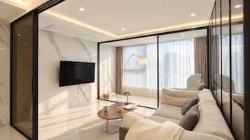 A modern living room with a large flat-screen TV, a sofa, a coffee table, and a window with curtains.