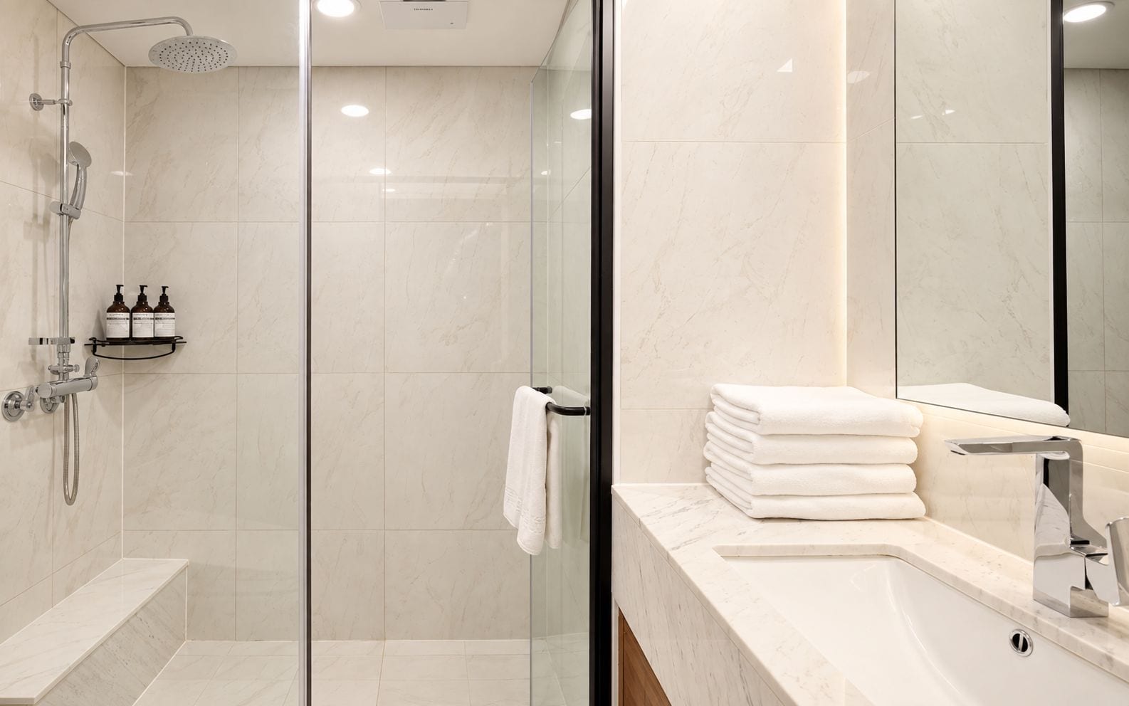 Een moderne badkamer met een douche in een glazen cabine, een wastafel met spiegel en een stapel witte handdoeken.
