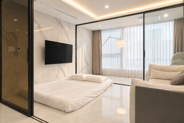 A modern hotel room with a bed, a sofa, a TV mounted on the wall, and a large window with curtains. - UH FLAT THE SEOCHO (Seoul)