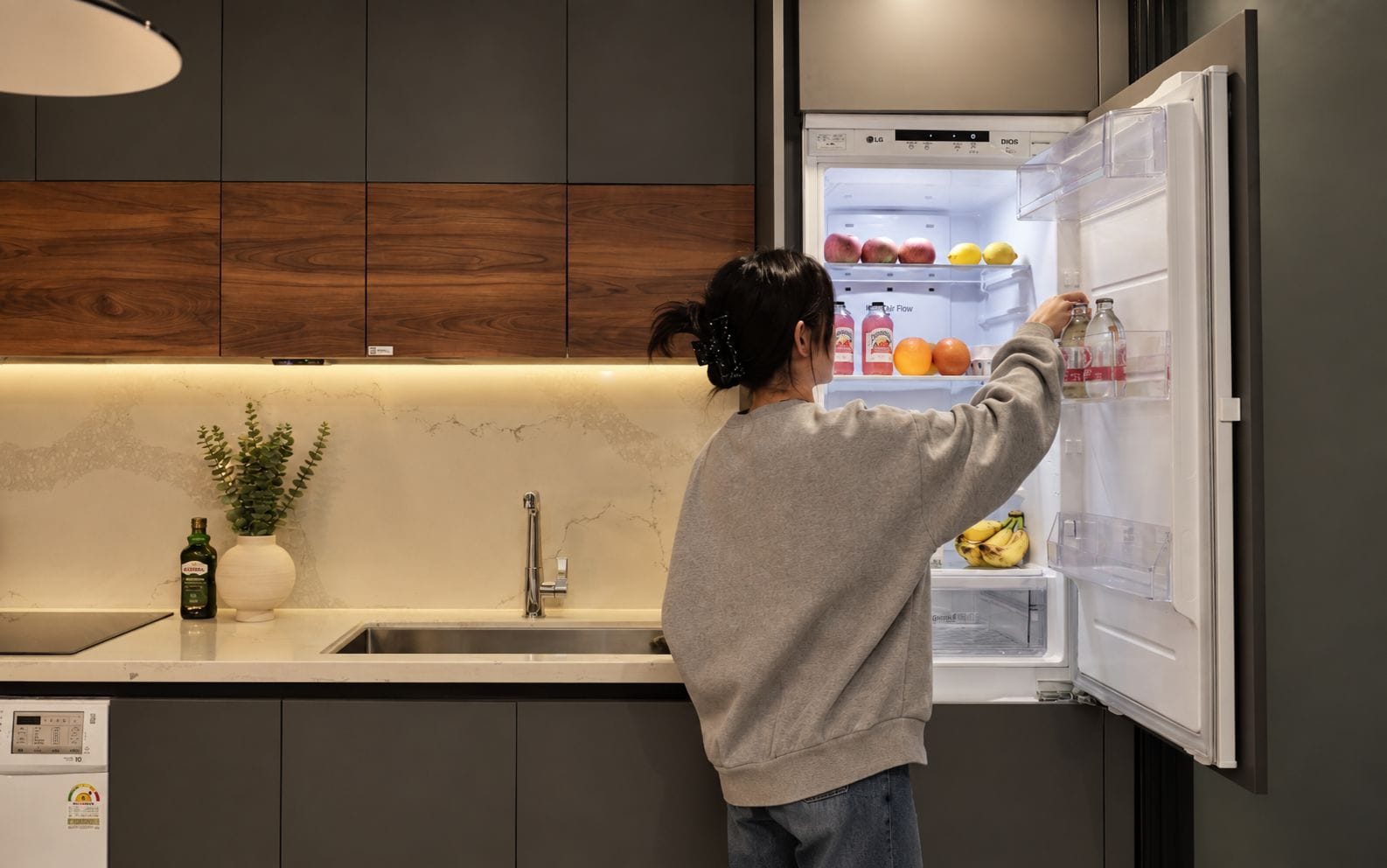 Una persona in cucina con un elettrodomestico moderno, un lavello e una pianta in vaso.
