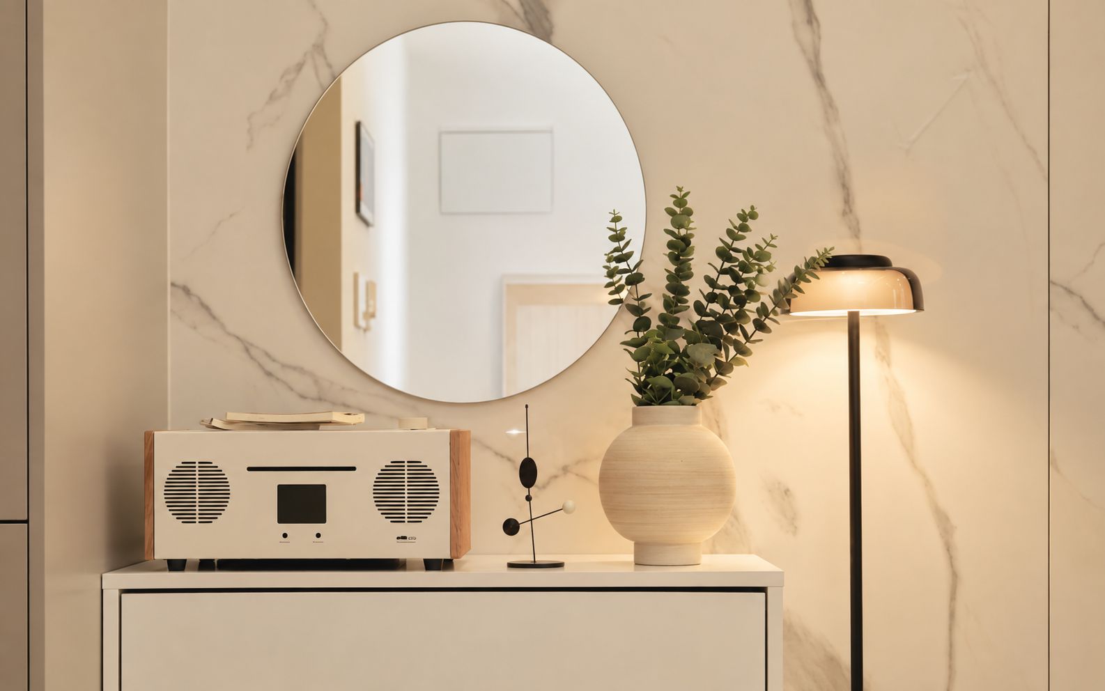 A modern bathroom vanity with a radio, a round mirror, and a vase with green plants.