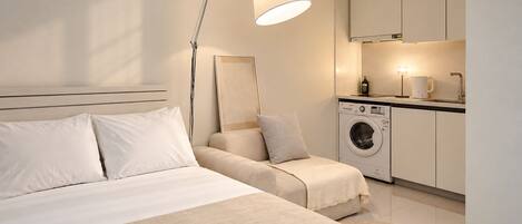 Un dormitorio moderno con cama, lámpara de noche y una zona de kitchenette con lavadora.