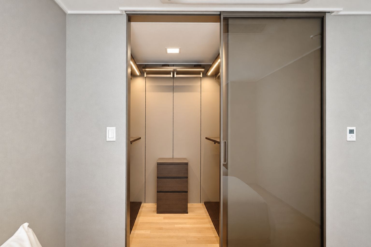 A modern, well-lit walk-in closet with a wooden bench and a sliding door.