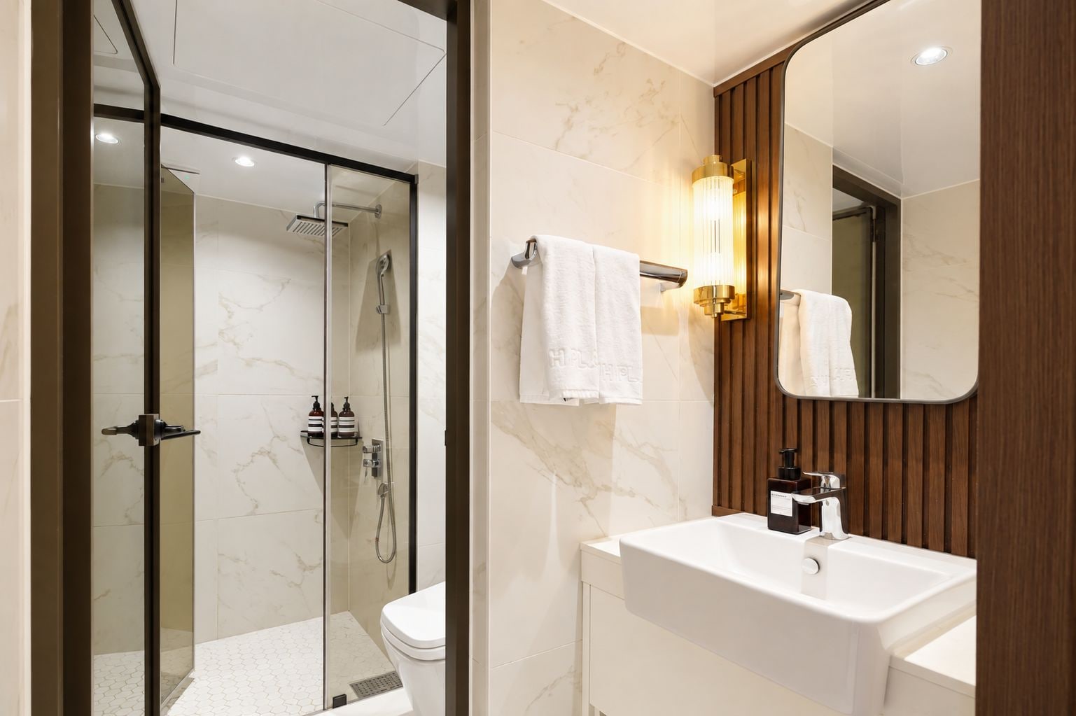 Un bany modern amb dutxa d'estuc de vidre, un lavabo blanc i un mirall amb panells de fusta.