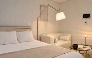 Habitación de hotel con cama, una silla, mesita de noche con lámpara y televisor montado en la pared.