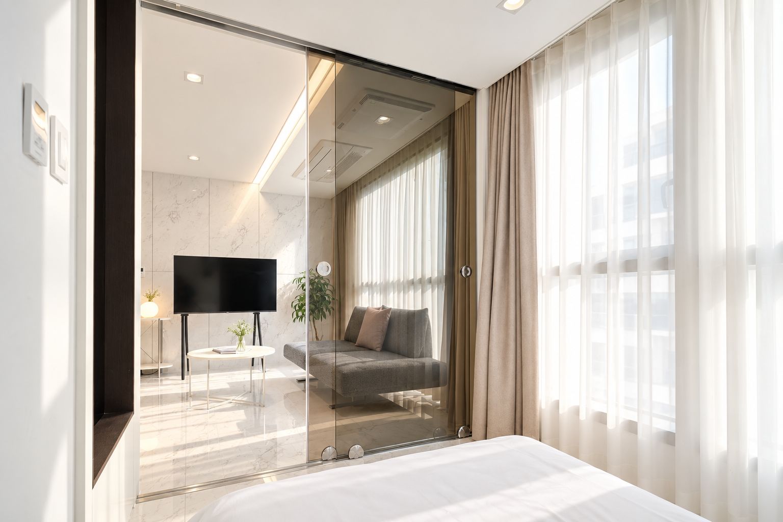Une chambre d’hôtel moderne dotée d’un grand lit, d’une télévision, d’un canapé et d’une cloison en verre.