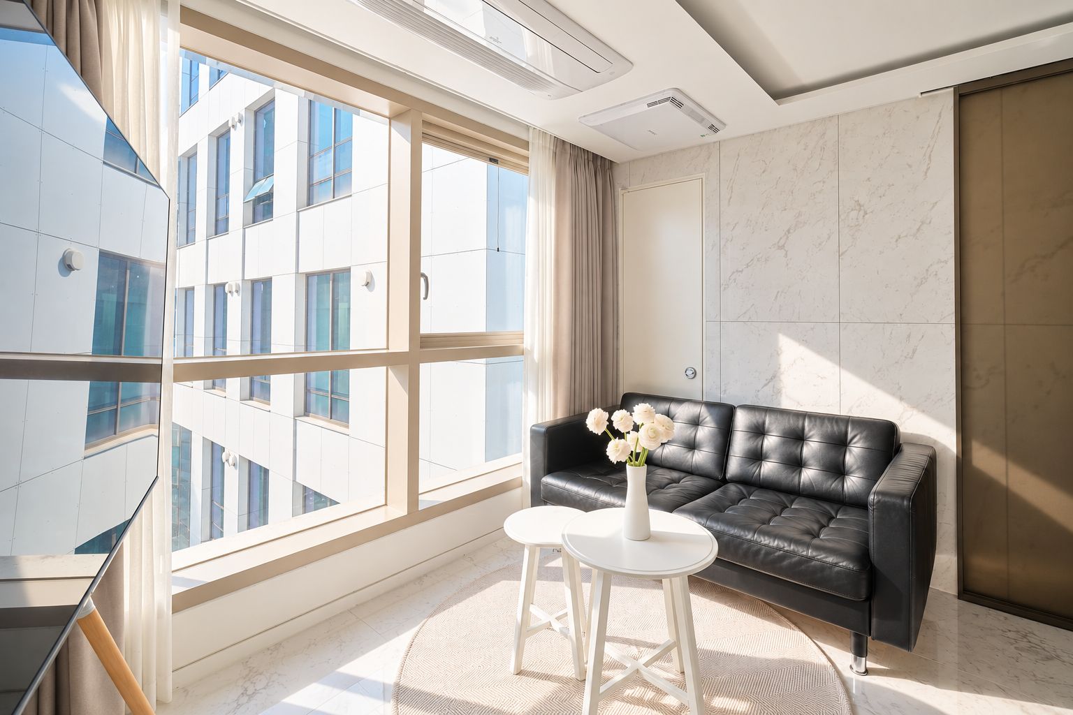 A modern living room with a black leather sofa, a white coffee table, and a vase of white flowers.