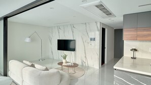 A modern living room with a sofa, a round coffee table, a TV, and a kitchen area with a marble countertop. - UH FLAT THE SEOCHO (Seoul)