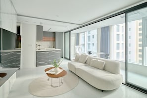 A modern living room with a sofa, a coffee table, and a view of a cityscape through large windows. - UH FLAT THE SEOCHO (Seoul)