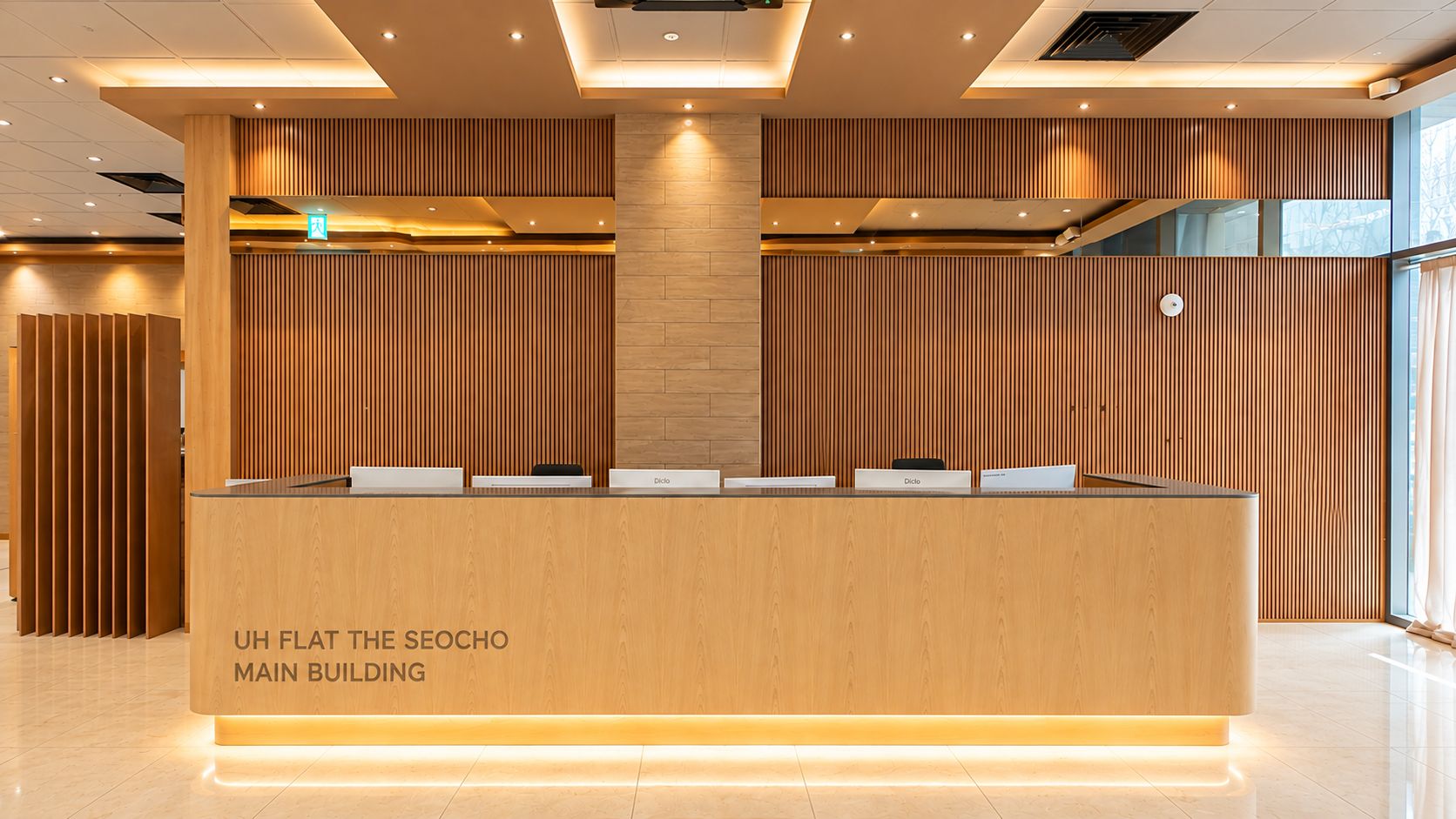Un comptoir d’accueil avec un revêtement en bois et l’inscription « UH FLAT THE SEOCHO MAIN BUILDING » à sa base.