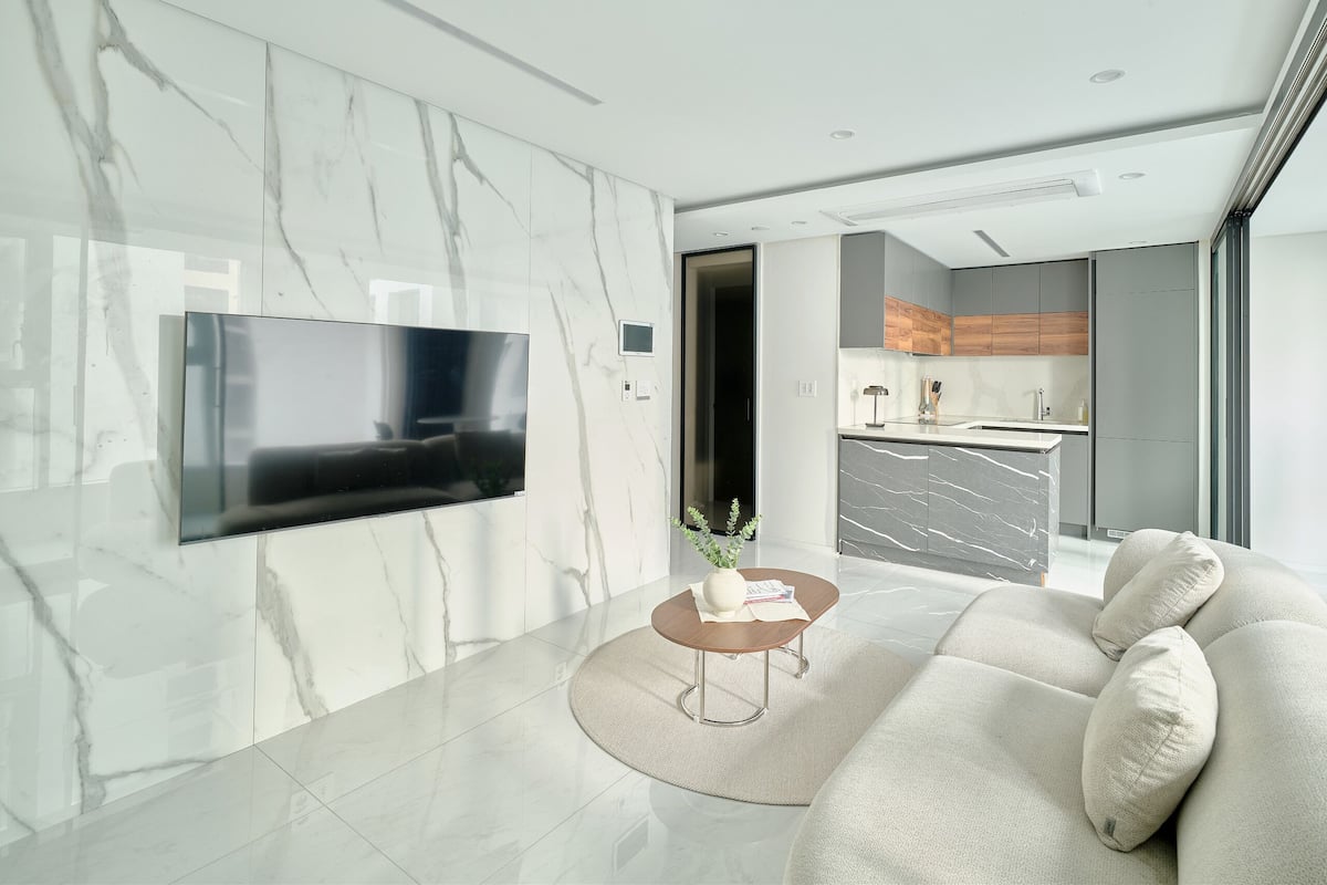 A modern living room with a flat-screen TV, a sofa, a coffee table, and a kitchen in the background.