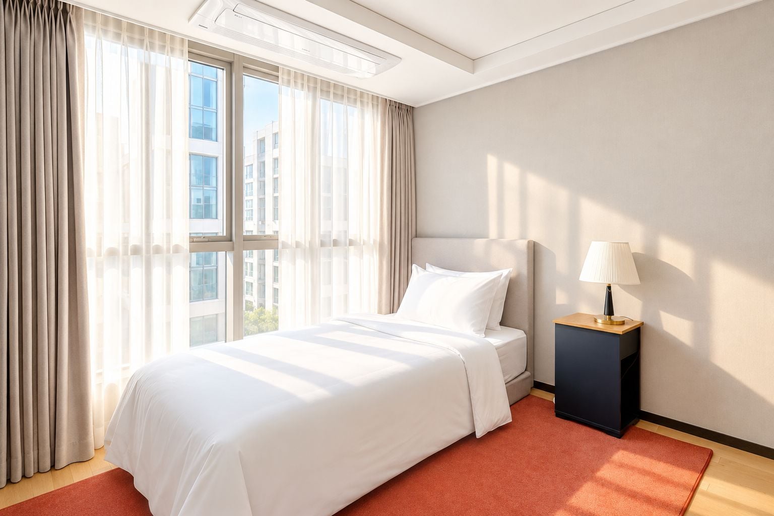 A hotel room with a large bed, a nightstand, a lamp, and a view of buildings through the window.