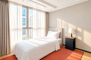 A hotel room with a large bed, a nightstand, a lamp, and a view of buildings through the window. - UH FLAT THE SEOCHO (Seoul)