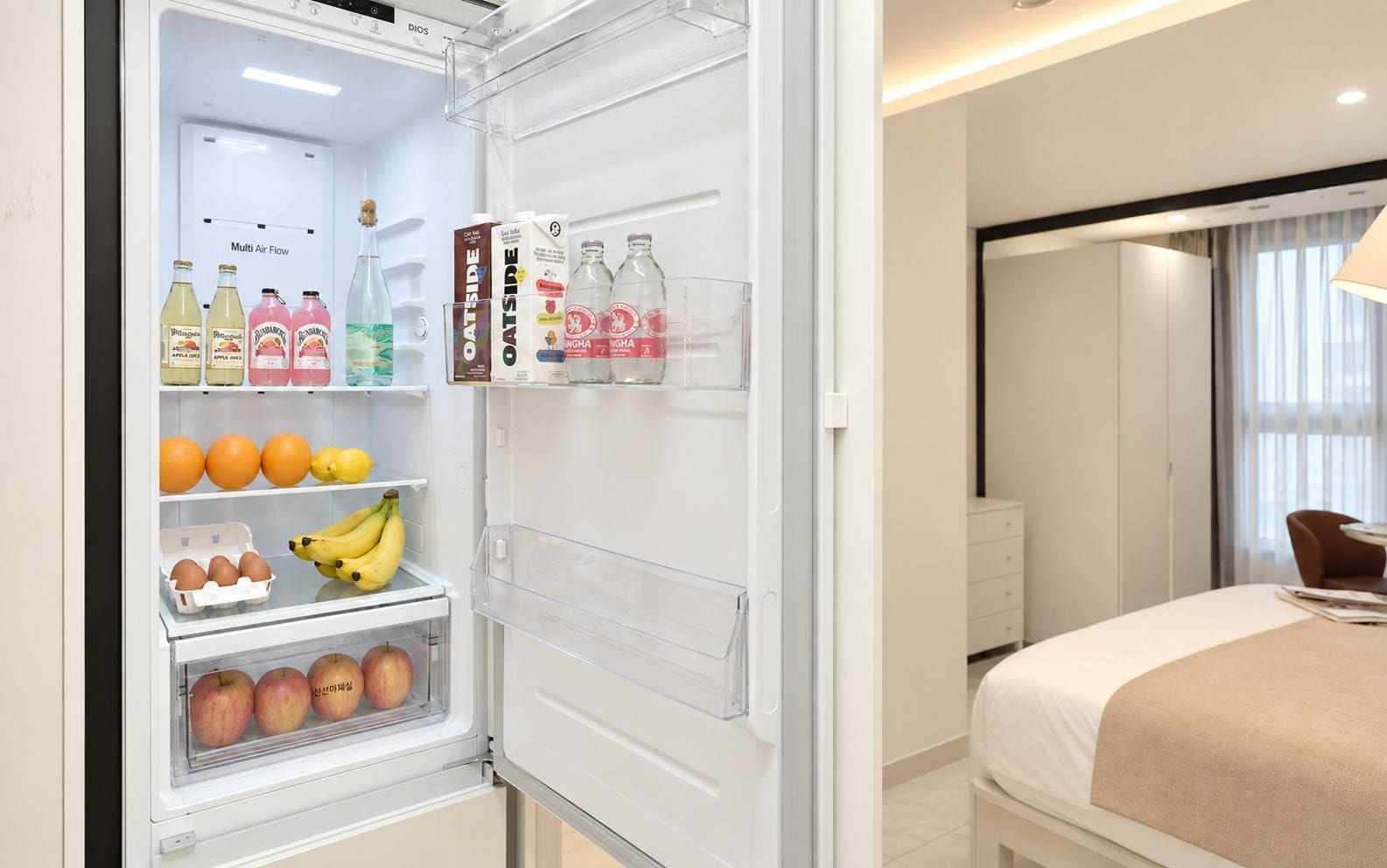 A hotel room with a minibar, a bed, a bedside table, and a window with curtains.