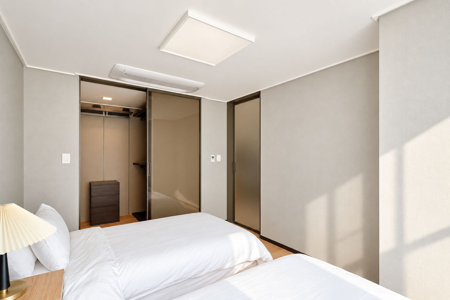 Une chambre d’hôtel moderne équipée d’un lit, d’une table de chevet, d’une lampe et d’un dressing avec des portes coulissantes.