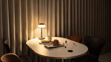 A round table with a lamp, a banana, a croissant, and a newspaper.