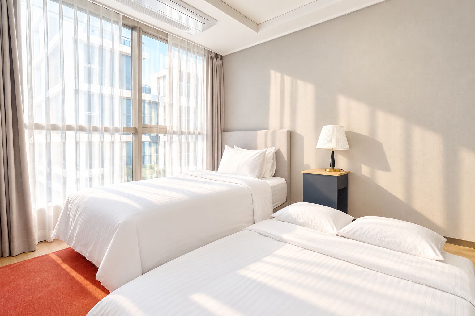 Habitación de hotel con dos camas, una mesita de noche con lámpara y un ventanal con cortinas.