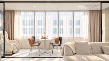 Un salon moderne avec un canapé, deux fauteuils, une table ronde et une grande fenêtre avec des rideaux.