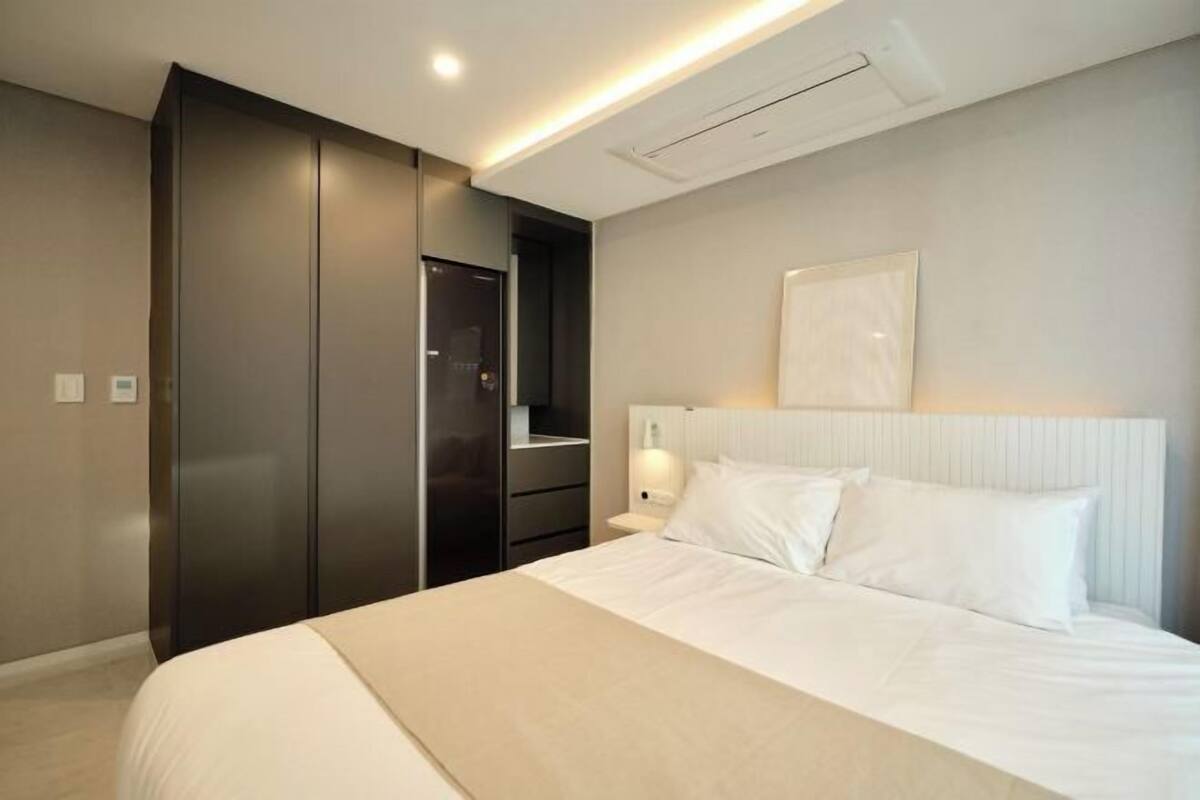 A bedroom with a bed, a wardrobe, a nightstand, and a wall-mounted light fixture.