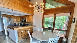 A modern kitchen with wooden cabinets, a central island with stools, and a dining area with a round table and chairs. - Beautiful Home w/ 2 fireplaces, Deck, and 75ft of Private Higgins Lake Frontage (Roscommon)