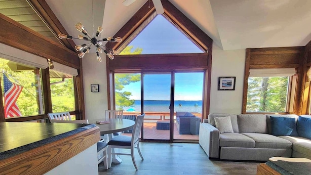 A spacious living area with a large sliding glass door leading to a balcony overlooking a body of water. - Beautiful Home w/ 2 fireplaces, Deck, and 75ft of Private Higgins Lake Frontage (Roscommon)