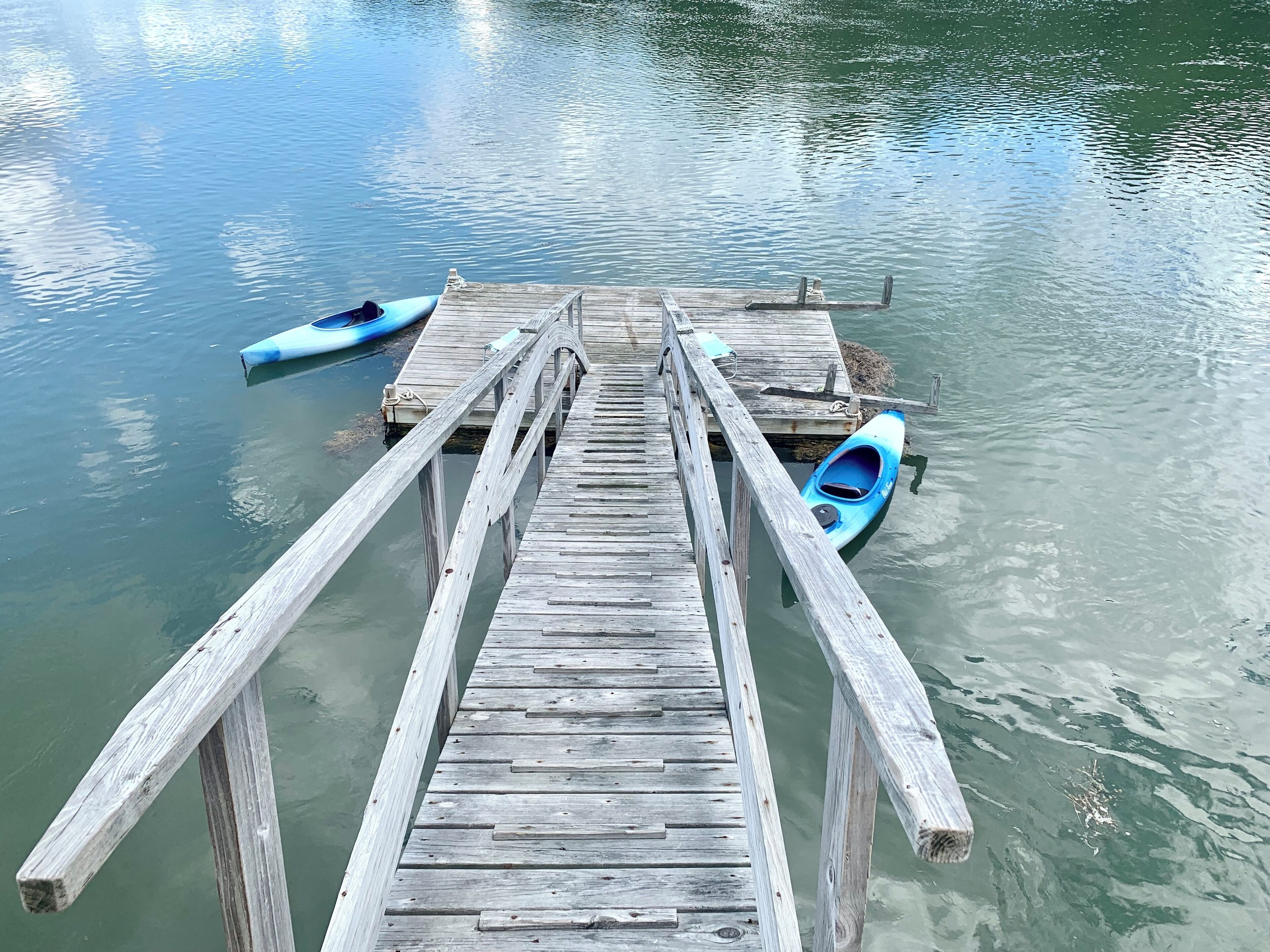 A wooden pier extending into calm water with two kayaks docked at the end.