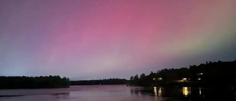 Vista nocturna de un lago tranquilo con un colorido despliegue de aurora boreal en el cielo.