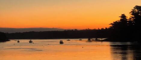 A calm body of water with several boats at sunset.