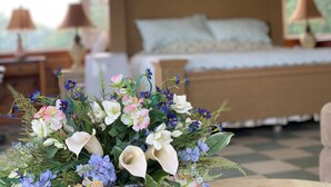 A bedroom with a wooden bed, a nightstand with a lamp, and a floral arrangement in the foreground. - Large beautiful ocean front studio with private dock (Harpswell)