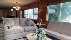 A cozy living room with a beige sofa, a matching armchair, and a marble coffee table. There is a chandelier hanging from the ceiling, and a window with a view of greenery outside. - Large beautiful ocean front studio with private dock (Harpswell)