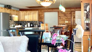 A modern kitchen with wooden cabinets, a dining area with a table and chairs, and a chandelier. - Large beautiful ocean front studio with private dock (Harpswell)