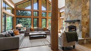 A spacious living room with a stone fireplace, large windows, and a cozy seating area. - Mountain view chalet w/ hot tub (Whistler)