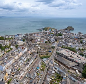An aerial view of a coastal town with a mix of residential and commercial buildings, a prominent rocky outcrop, and a clear view of the sea. - Penlan - Close to Town and Beaches (Tenby)